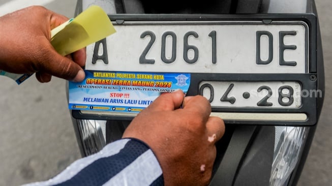 Polisi menempelkan stiker keselamatan berlalu lintas pada plat sepeda motor saat Operasi Zebra Maung 2024 di Kota Serang, Banten, Selasa (15/10/2024). [ANTARA FOTO/Muhammad Bagus Khoirunas/nym]
