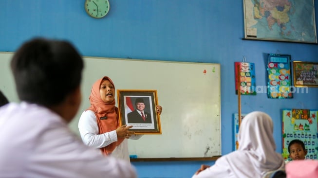 Guru memperlihatkan bingkai foto presiden Prabowo Subianto dan wakil presiden Gibran Rakabuming Raka kepada murid di SDN Pondok Labu 14 Pagi, Jakarta, Selasa (22/10/2024). [Suara.com/Alfian Winanto]