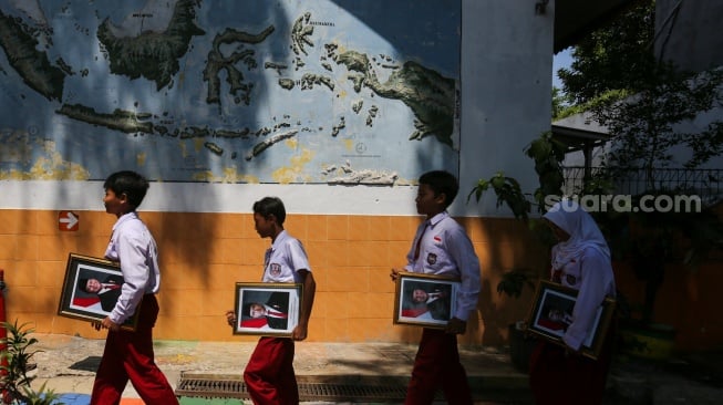 Pelajar membawa bingkai foto presiden Prabowo Subianto dan wakil presiden Gibran Rakabuming Raka di SDN Pondok Labu 14 Pagi, Jakarta, Selasa (22/10/2024). [Suara.com/Alfian Winanto]