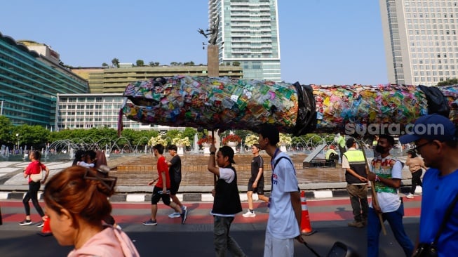 Aktivis lingkungan dari komunitas Aksi Muda Jaga Iklim membawa replika paus dan naga yang terbuat dari sampah plastik di kawasan Bundaran HI, Jakarta, Minggu (27/10/2024). [Suara.com/Alfian Winanto]