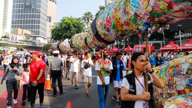 Aktivis lingkungan dari komunitas Aksi Muda Jaga Iklim membawa replika paus dan naga yang terbuat dari sampah plastik di kawasan Bundaran HI, Jakarta, Minggu (27/10/2024). [Suara.com/Alfian Winanto]