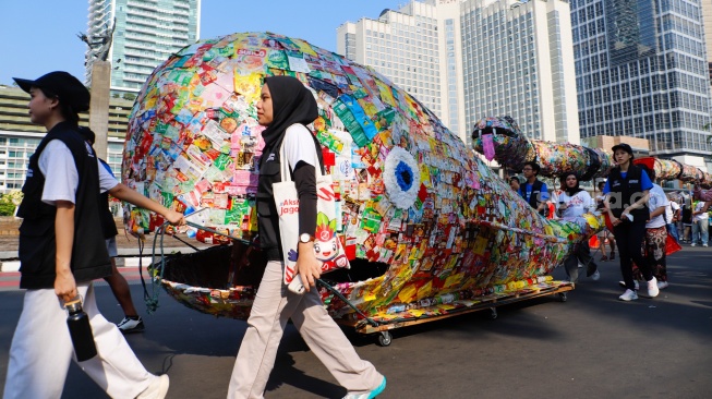 Aktivis lingkungan dari komunitas Aksi Muda Jaga Iklim membawa replika paus dan naga yang terbuat dari sampah plastik di kawasan Bundaran HI, Jakarta, Minggu (27/10/2024). [Suara.com/Alfian Winanto]