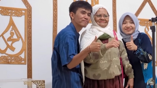 Ibu Eny membawa tas saat berfoto dengan anak dan menantunya, Tiko dan Nadiyah. (YouTube/TIKO)