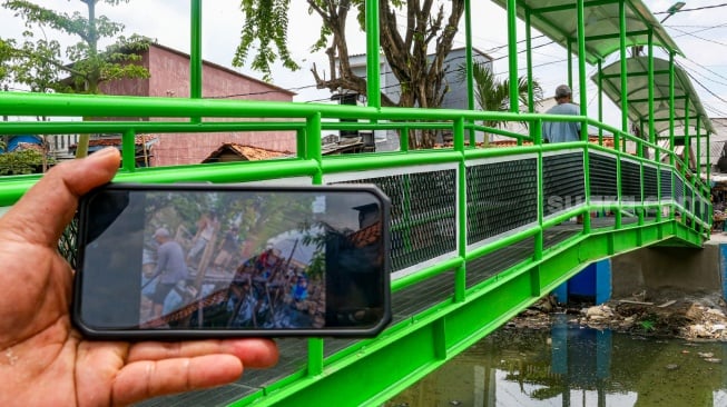 Aktivitas warga saat melewati jembatan Ijo di kawasan Batu Tumbuh, Jakarta, Rabu (13/11/2024). [Suara.com/Alfian Winanto]