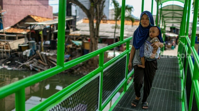 Aktivitas warga saat melewati jembatan Ijo di kawasan Batu Tumbuh, Jakarta, Rabu (13/11/2024). [Suara.com/Alfian Winanto]