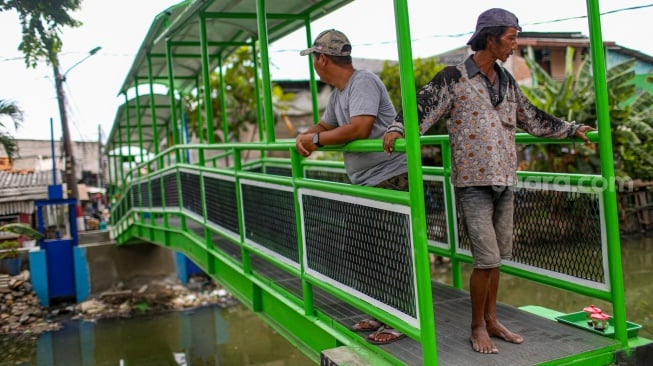 Aktivitas warga saat melewati jembatan Ijo di kawasan Batu Tumbuh, Jakarta, Rabu (13/11/2024). [Suara.com/Alfian Winanto]