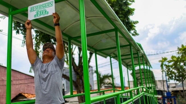 Aktivitas warga saat melewati jembatan Ijo di kawasan Batu Tumbuh, Jakarta, Rabu (13/11/2024). [Suara.com/Alfian Winanto]