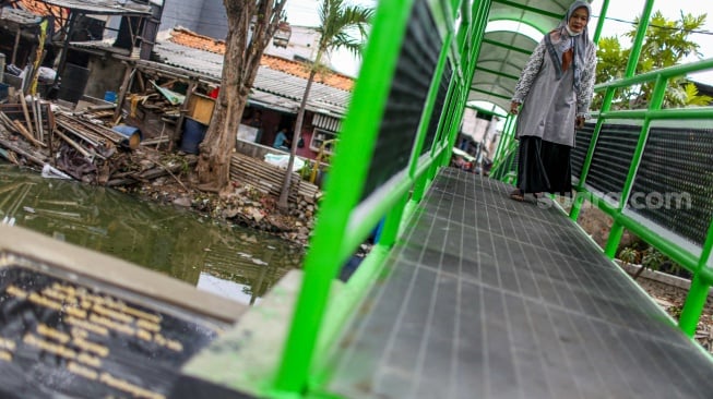 Aktivitas warga saat melewati jembatan Ijo di kawasan Batu Tumbuh, Jakarta, Rabu (13/11/2024). [Suara.com/Alfian Winanto]