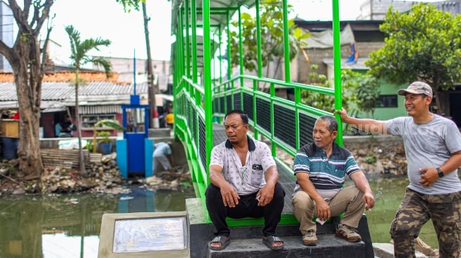 Aktivitas warga saat melewati jembatan Ijo di kawasan Batu Tumbuh, Jakarta, Rabu (13/11/2024). [Suara.com/Alfian Winanto]