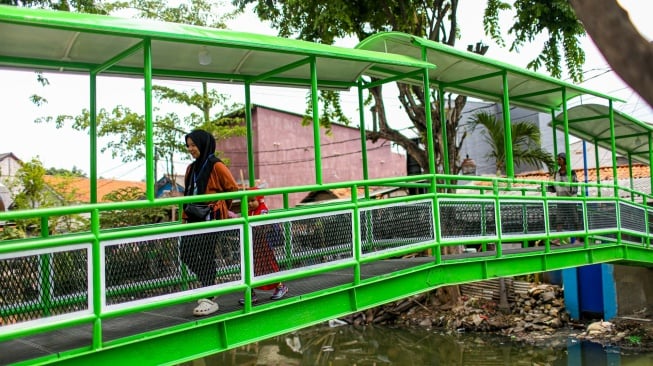 Aktivitas warga saat melewati jembatan Ijo di kawasan Batu Tumbuh, Jakarta, Rabu (13/11/2024). [Suara.com/Alfian Winanto]