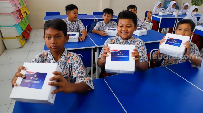 Para siswa menerima kotak makan saat mengikuti uji coba Program Makan Bergizi gratis di SD Angkasa 5 Halim Perdana Kusuma, Jakarta, Selasa (26/11/2024). [Suara.com/Alfian Winanto]