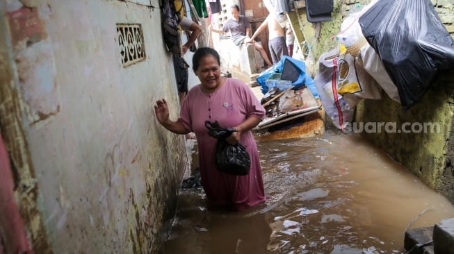 Warga beraktivitas di tengah banjir yang menggenang di wilayah Kebon Pala, Jakarta, Kamis (28/11/2024). [Suara.com/Alfian Winanto]
