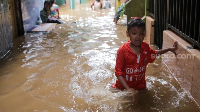 Warga beraktivitas di tengah banjir yang menggenang di wilayah Kebon Pala, Jakarta, Kamis (28/11/2024). [Suara.com/Alfian Winanto]
