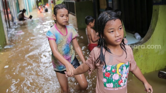 Warga beraktivitas di tengah banjir yang menggenang di wilayah Kebon Pala, Jakarta, Kamis (28/11/2024). [Suara.com/Alfian Winanto]
