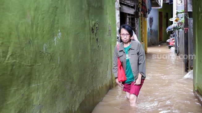 Warga beraktivitas di tengah banjir yang menggenang di wilayah Kebon Pala, Jakarta, Kamis (28/11/2024). [Suara.com/Alfian Winanto]
