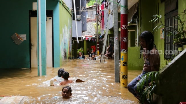 Warga beraktivitas di tengah banjir yang menggenang di wilayah Kebon Pala, Jakarta, Kamis (28/11/2024). [Suara.com/Alfian Winanto]
