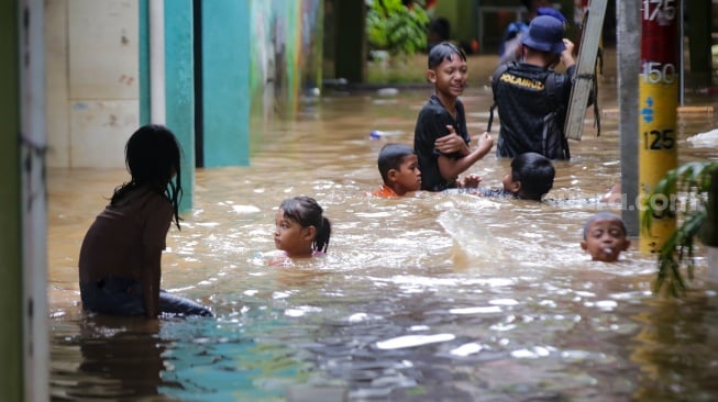 Warga beraktivitas di tengah banjir yang menggenang di wilayah Kebon Pala, Jakarta, Kamis (28/11/2024). [Suara.com/Alfian Winanto]
