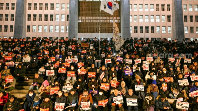 Orang-orang menyerukan pengunduran diri Presiden Korea Selatan Yoon Suk Yeol saat mereka mengambil bagian dalam protes di tangga menuju Majelis Nasional di Seoul, Korea Selatan, Rabu (4/12/2024). [Anthony WALLACE / AFP]