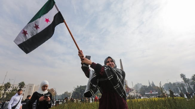 Seorang wanita mengibarkan bendera oposisi Suriah saat merayakan kemenangan di Lapangan Umayyah di Damaskus, Suriah, Minggu (8/12/2024). [Bakr AL KASSEM / AFP]