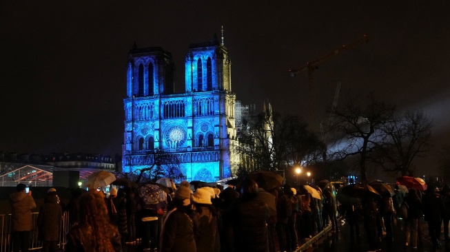 Kerumunan orang berdiri saat lampu-lampu dinyalakan dalam upacara pembukaan kembali Katedral Notre Dame di Paris, Prancis, Minggu (8/12/2024). [Dimitar DILKOFF / AFP]