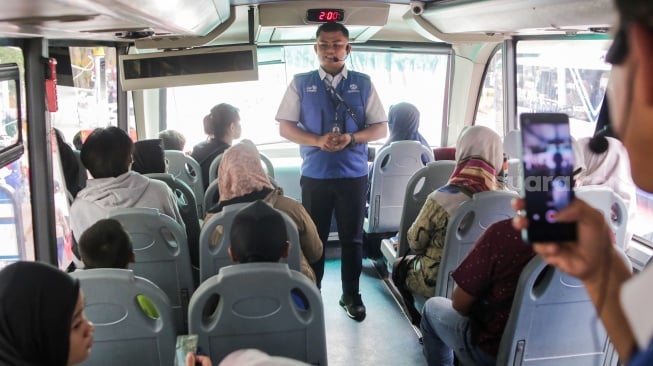 Petugas memberikan penjelas kepada warga yang menaiki bus tingkat wisata TransJakarta di kawasan Monas, Jakarta, Kamis (26/12/2024). [Suara.com/Alfian Winanto]