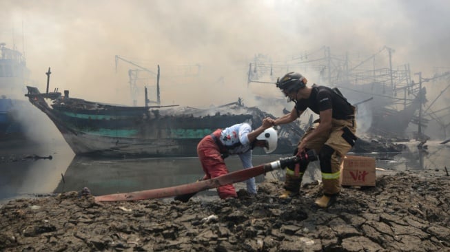 Petugas terperosok saat berusaha memadamkan kapal nelayan yang terbakar di Pelabuhan Tegal, Jawa Tengah, Jumat (27/12/2024). [ANTARA FOTO/Oky Lukmansyah/nym]