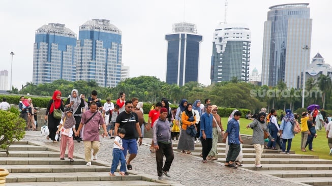 Pengunjung berwisata di kawasan Monas, Jakarta, Jumat (27/12/2024). [Suara.com/Alfian Winanto]