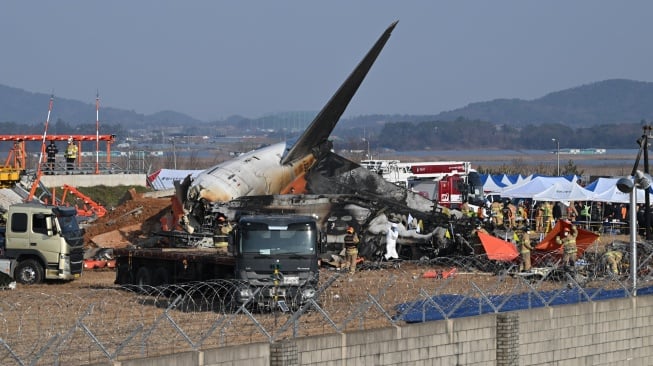 Petugas pemadam kebakaran dan petugas penyelamat bekerja di dekat reruntuhan pesawat Boeing 737-800 seri Jeju Air setelah pesawat itu jatuh dan terbakar di Bandara Internasional Muan di Provinsi Jeolla Selatan, Korea Selatan, Senin  (30/12/2024). [YONHAP / AFP]