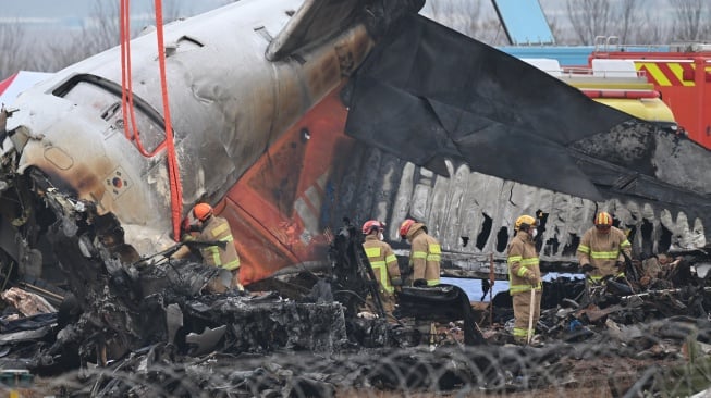 Bagian ekor pesawat Boeing 737-800 Jeju Air yang jatuh dan terbakar terlihat di ujung landasan pacu di Bandara Internasional Muan di Provinsi Jeolla Selatan, Korea Selatan, Senin (30/12/2024). [YONHAP / AFP]