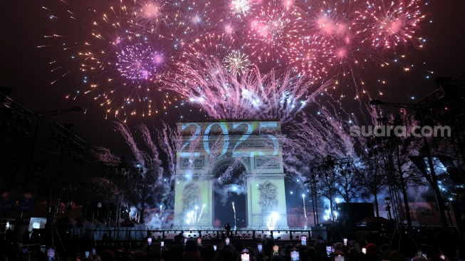 Kembang api menerangi langit di sekitar Arc de Triomphe di Avenue des Champs-Elysees di Paris, Prancis, Rabu (1/1/2025). [Thomas SAMSON / AFP]