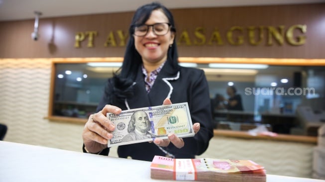 Petugas salah satu tempat penukaran mata uang asing menunjukkan uang rupiah dan dolar AS, Jakarta, Selasa (14/1/2025). [Suara.com/Alfian Winanto]