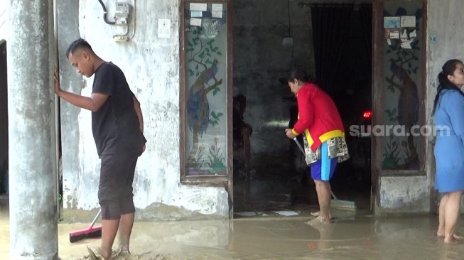 Warga Desa Tlogoweru, Kecamatan Guntur, Demak membersihkan lumpur yang terbawa banjir, Selasa (21/01/2025). (suara.com/Sigit AF)