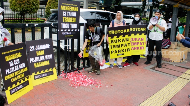 Aktivis dari Koalisi Pejalan Kaki menggelar aksi tabur bunga di Halte Tugu Tani, Jakarta, Rabu (22/1/2025). [Suara.com/Alfian Winanto