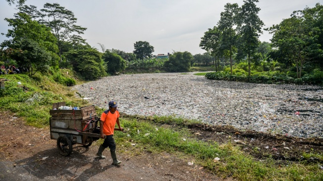 Petugas kebersihan melintas di samping tumpukan sampah yang menumpuk di Sungai Citarum Lama, di Cicukang, Margaasih, Kabupaten Bandung, Jawa Barat, Senin (27/1/2025). [ANTARA FOTO/Raisan Al Farisi/foc]