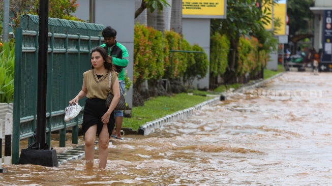 Warga melintasi banjir di Jalan Boulevard Raya, Kelapa Gading, Jakarta, Rabu (29/1/2025). [Suara.com/Alfian Winanto]