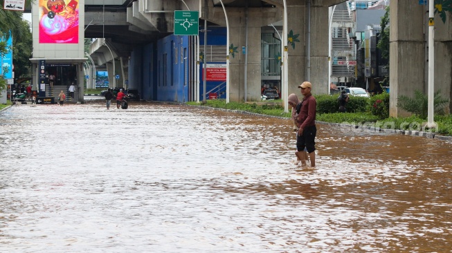 Warga melintasi banjir di Jalan Boulevard Raya, Kelapa Gading, Jakarta, Rabu (29/1/2025). [Suara.com/Alfian Winanto]