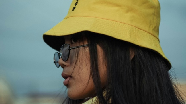 Ilustrasi wanita memakai aksesoris topi ember (bucket hat) dan kaca mata. [pexels.com/Chris Creatives]