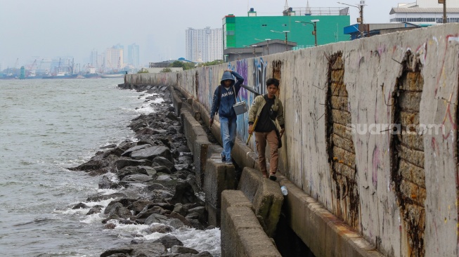 Warga beraktivitas di sekitar tanggul laut kawasan muara baru, Jakarta, Rabu (5/2/2025). [Suara.com/Alfian Winanto]