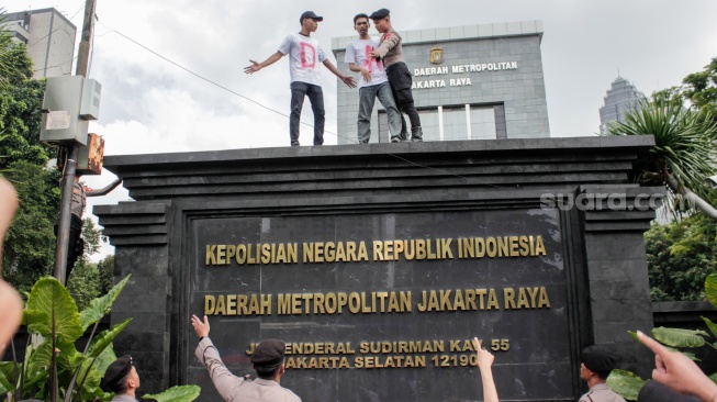 Massa dari Aliansi Rakyat Menggugat (ARM) menaiki dinding saat menggelar aksi unjuk rasa di depan Polda Metro Jaya, Jakarta, Jumat (7/2/2025). [Suara.com/Alfian Winanto]