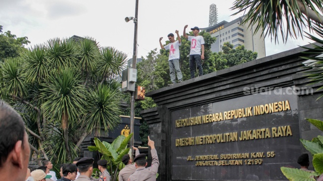 Massa dari Aliansi Rakyat Menggugat (ARM) menaiki dinding saat menggelar aksi unjuk rasa di depan Polda Metro Jaya, Jakarta, Jumat (7/2/2025). [Suara.com/Alfian Winanto]