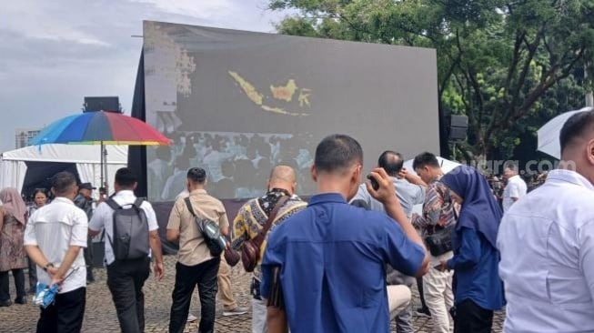 Penampakan warga menonton gladi bersih pelantikan kepala daerah di Monas lewat videotron. 