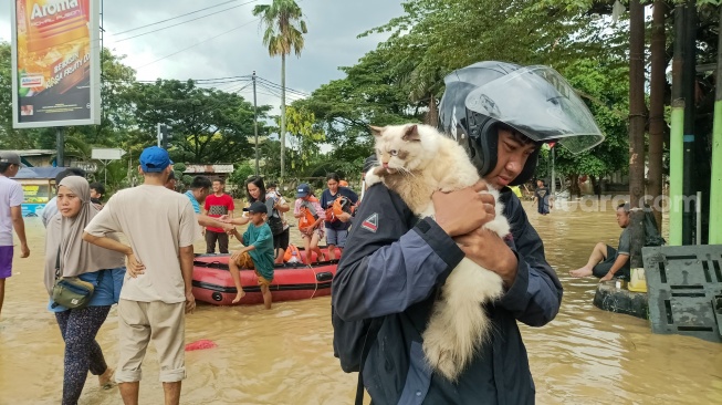 Warga dan kucingnya berjalan usai dievakuasi dari banjir di Kawasan Grand Galaxy City, Kota Bekasi, Jawa Barat, Selasa (4/3/2025). [Suara.com/Alfian Winanto]