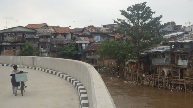 Warga melintas di samping Sungai Ciliwung, Jakarta. Normalisasi Ciliwung terus dilakukan Pemprov Jakarta untuk mengantisipasi banjir. [Suara.com]