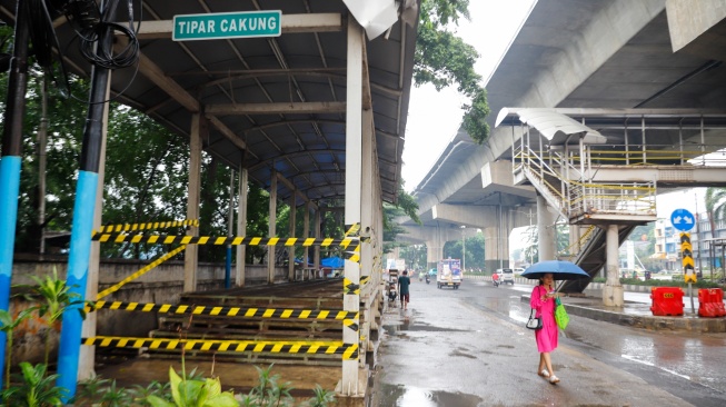 Warga melintas di samping Halte dan Jembatan Penyeberangan Orang (JPO) Tipar Cakung yang rusak di Jakarta, Sabtu (26/4/2025). [Suara.com/Alfian Winanto]
