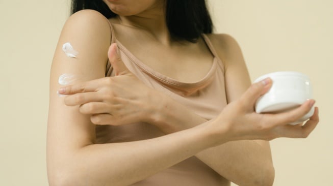 Ilustrasi wanita memakai body serum / body lotion di tangan. [Pexels/SHVETS production]