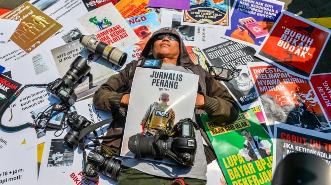 Seorang jurnalis merebahkan diri di atas poster saat melakukan aksi memperingati Hari Buruh di Taman Cikapayang, Bandung, Jawa Barat, Kamis (1/5/2025). [ANTARA FOTO/Raisan Al Farisi/tom]