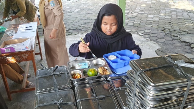 Seorang siswa SDN Kledokan mengambil menu MBG ketika ruang kelasnya ambrol, Senin (5/5/2025). [Hiskia Andika Weadcaksana/Suarajogja.id]