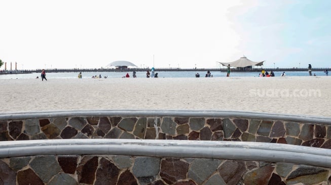 Pengunjung berwisata di Pantai Lagoon, Taman Impian Jaya Ancol, Jakarta, Selasa (13/5/2025). [Suara.com/Alfian Winanto]