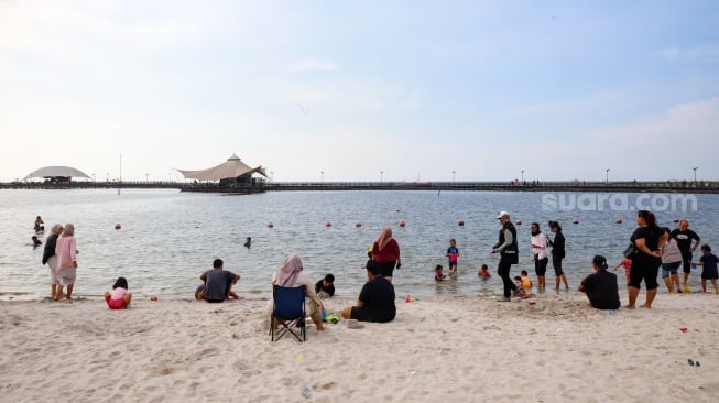 Pengunjung berwisata di Pantai Lagoon, Taman Impian Jaya Ancol, Jakarta, Selasa (13/5/2025). [Suara.com/Alfian Winanto]