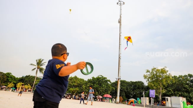 Pengunjung berwisata di Pantai Lagoon, Taman Impian Jaya Ancol, Jakarta, Selasa (13/5/2025). [Suara.com/Alfian Winanto]